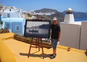 Сын у картины на крыше дома острова Санторин в Греции
